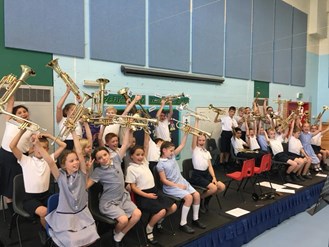 The pupils of Grangefield Primary sat on stage, holding their brass instruments up in the air