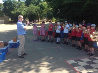 The pupils of Stratton Primary stood in a semicircle, performing in their brass concert, with their teacher stood facing them
